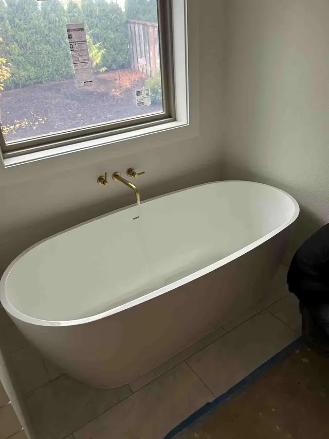 Freestanding soaking tub with wall-mount gold faucet by picture window in Welches OR – Efficiency Plumbing
